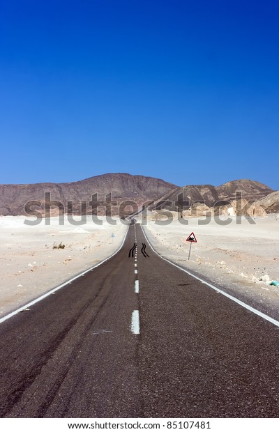 A straight road through the desert\
disappears towards the mountains in the\
distance