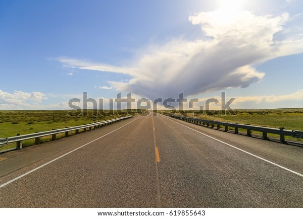 Straight road with two cars in the back\
running through\
grassland.