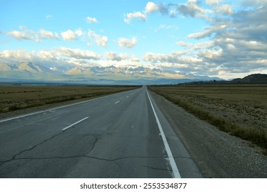 A straight two-lane paved road crosses the edgeless steppe to meet snow-capped mountain ranges on a sunny summer morning. Chuysky Tract, Altai, Siberia, Russia. - Powered by Shutterstock