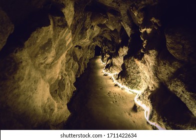 Straight Underground Path In A Stone Cave Illuminated By Yellow Light With Rock Wall And A Black Hole At The End