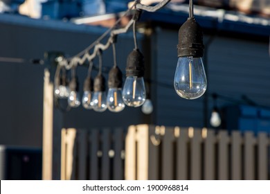 A Strand Of Vintage-style Light Bulbs Hanging Up At An Outdoor Event Space In The Daytime