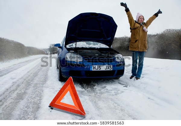 Stranded woman
is trying to flag down another car next to her broken down car on a
cold, snowy day to help her
out.