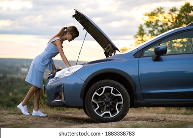 Stranded Young Woman Driver Standing Near A Broken Car With Popped Up Bonnet Inspecting Her Vehicle Motor.