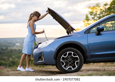 Stranded Young Woman Driver Standing Near A Broken Car With Popped Up Bonnet Inspecting Her Vehicle Motor.