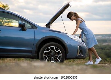 Stranded Young Woman Driver Standing Near A Broken Car With Popped Up Bonnet Inspecting Her Vehicle Motor.