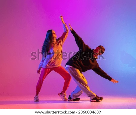 Strange body movements. Two young people, guy and girl dancing contemporary dance over pink background in neon light. Modern dance aesthetics concept