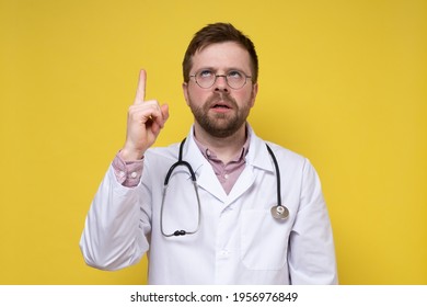 Strange Doctor Raised Index Finger And Eyes Upward, He Thought And Tried To Remember Something. Yellow Background.