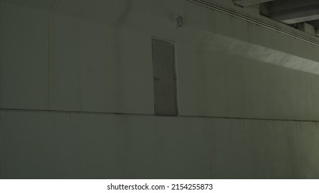 Strange door beneath bridge, with light streaming in from the side. Leading lines, on an empty wall.