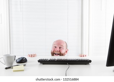 Strange And Happy Office Worker Looking Up From Under His Desk. Hiding Behind His Desk.