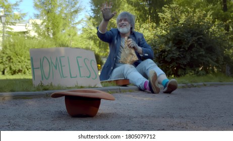 Strangers Giving Money To Homeless Beggar Sitting On Ground In City Park. Poor Old Man Waving Hand Thanking Eople For Putting Banknotes In Hat Sitting On Street With Cardboard Sign