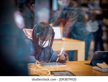 Strasbourg, France - Dec 17, 2021: View From The Street Of Young Black Ethnicity Girl Wearing White Mask Looking At Latest IPad Computer Tablet Inside Apple Computers Store - Using Apple Pencil Input