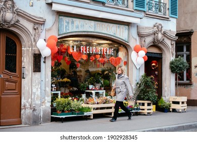 Strasbourg, France - Feb 14, 2019: Single woman walking near Fleurs Broglie La Fleuristerie florist store shop showcase decorated with multiple hearts during Saint Valentine day