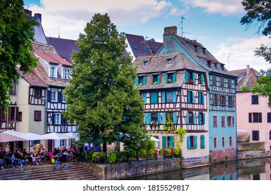Strasbourg / France - July 11, 2020: Colorful half-timbered houses and a restaurant with an outdoor area at a canal in the historical city of Strasbourg. The house facades reflect in the water.