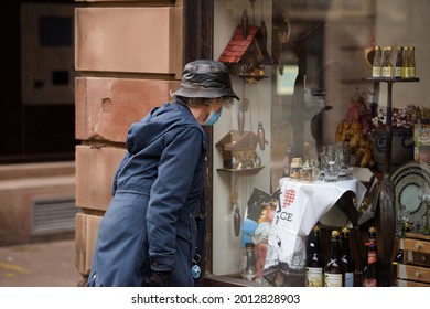 Strasbourg, France - May 20, 2021: Side View Of Curious Senior Woman Looking At The Showcase Of An Antique Souvenir Store Selling Diverse Memorabilia From Alsace Region