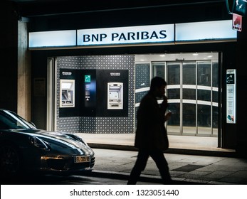 Strasbourg, France - Oct 14, 2017: Male Silhouette Walking In Front Of BNP Paribas Headquarters At Dusk With Two ATM's Bank Teller Mac And Parked Porsche Super Car In Frontines  