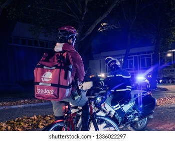 Strasbourg, France - Oct 27, 2018: Night Street Scene With Police Officer Blocking The Street - Foodora Cyclist Delivering Food Waiting Due To Official Delegation Visit