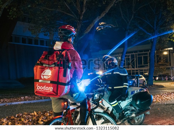 Strasbourg, France - Oct 27, 2018: Male police\
officer blocking the street - Foodora cyclist delivering food\
waiting due to official delegation\
visit