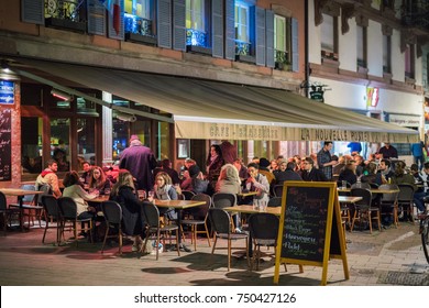 STRASBOURG, FRANCE - OCT 31, 2017: Customers Eating Drinkiing Outside On A Cold Night At The La Nouvelle Poste Cafe Bar Terrace In Strasbourg, France 