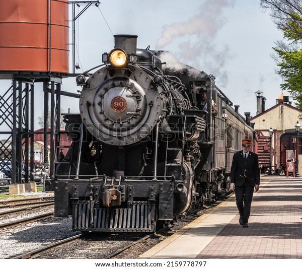 Strasburg Pennsylvania-April 22, 2022: Train\
conductor walks next to steam train as it arrives station in\
Strasburg, Lancaster County,\
Pennsylvania