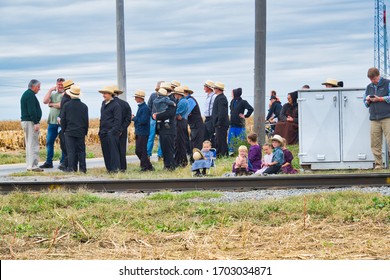 STRASBURG, UNITED STATES - Oct 13, 2019: Strasburg, Pennsylvania, October 2019 - Group of Amish men women and children patiently wait for a train to pass along train tracks on a fall day.