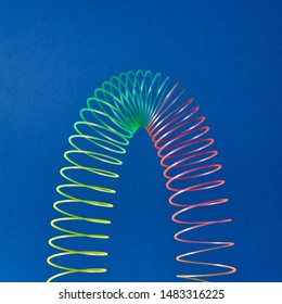 Stratching colorful toy spiral in the shape of parabola on a blue background with copy space.