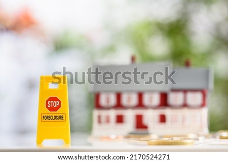 Strategies or ways to stop foreclosure or avoid foreclosure, mortgage relief, financial concept : Yellow sign board with the words STOP FORECLOSURE, a red-white two story house with coins on a table.