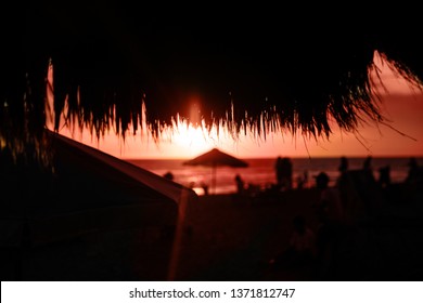 Straw beach roof in the cafe with blurred people on coral sunset. Summer concept.