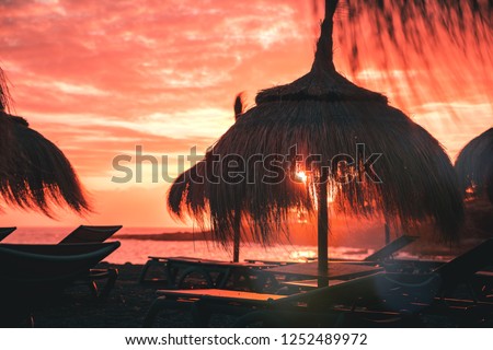 Straw beach umbrella at peach coral sunset
