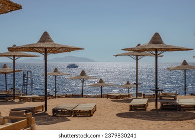 Straw beach umbrellas and wooden sun loungers under the blue sky at a beach with a sea in the background on a sunny day. - Powered by Shutterstock