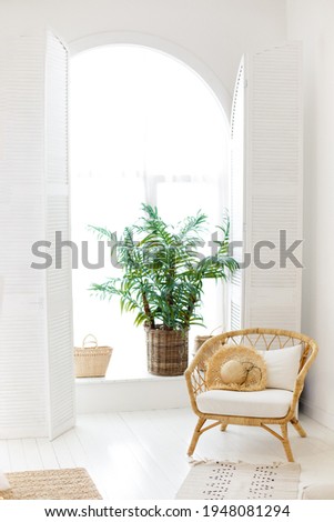 Straw chair in a light gray room in Boho style. Asian style room. Clean and simple interior. Plants in a room. Beach dwelling interior. Apartment for sea vacation