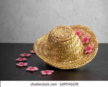 Straw Cow Girl Hat Sitting On A Black Slate Counter With Pink Felt Flowers Decorating It And A Gray Plaster Wall.  Fashion Accessory With Flowers.