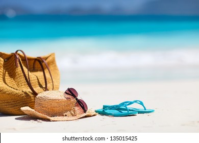 Chapeau de paille, sac, lunettes de soleil et tongs sur une plage tropicale