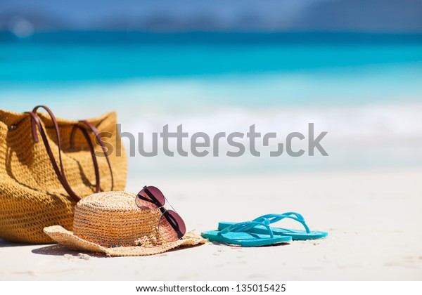 Straw hat, bag, sun glasses and flip flops on a\
tropical beach