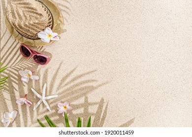 Straw Hat With Frangipani Flowers, Sea Shells And Sunglasses On White  Sand,  With Palm Tree Shadow. 