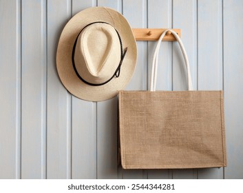 A straw hat hangs elegantly on a wooden peg beside a large burlap tote bag against a light blue wall, showcasing a minimalist and chic indoor decor style. - Powered by Shutterstock