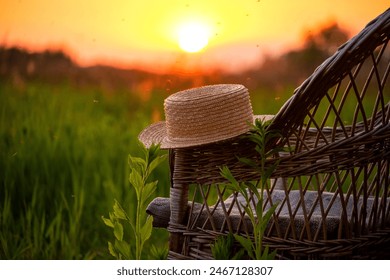 straw hat on an old wicker chair in a field overlooking the sunset on a summer evening.