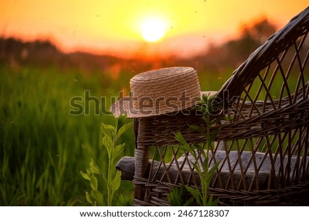 straw hat on an old wicker chair in a field overlooking the sunset on a summer evening.