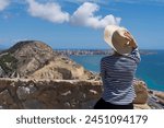 Straw hat, striped sweater, woman in hat (rear view). She is looking at Mirador (viewpoint) de la Sangueta. Alicante, Spain, typical sunny day at Mediterranean sea