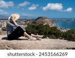 Straw hat, striped sweater, woman in hat (rear view). She is looking at Mirador (viewpoint) de la Sangueta, Alicante. View from Santa Barbara castle. 