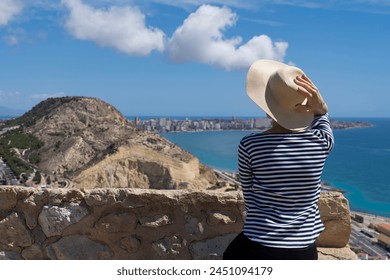 Straw hat, striped sweater, woman in hat (rear view). She is looking at Mirador (viewpoint) de la Sangueta. Alicante, Spain, typical sunny day at Mediterranean sea - Powered by Shutterstock