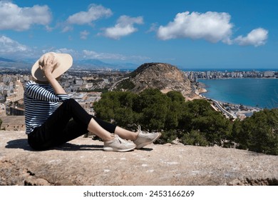 Straw hat, striped sweater, woman in hat (rear view). She is looking at Mirador (viewpoint) de la Sangueta, Alicante. View from Santa Barbara castle.  - Powered by Shutterstock