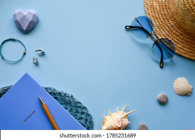 Straw hat, sunglasses, notepad with wooden pen, string bag, women's jewelry, seashells and pebbles on a blue paper background.  Top view. Flat lay. Summer background. Stock Photo