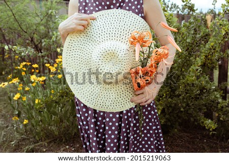 straw hatand a bouquet of tiger lily (lilium lancifolium) in hands of woman. Summer and travel concept.