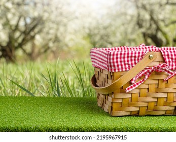 A Straw Picnic Basket On A Green Lawn Against The Backdrop Of Stunning Nature. Camping, Picnic, Romantic Date, Delicious Food And Drinks. Advertising, Banner, Invitation.