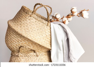 Straw wicker basket, natural cotton fabric, cotton flower branch on gray background. Bamboo basket stylish interior item eco design handmade. Decor of home. Natural eco materials, storage basket