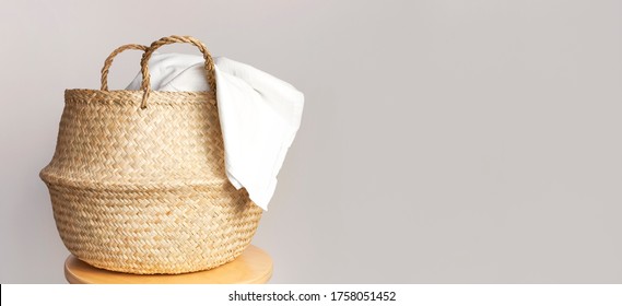 Straw wicker basket and white natural cotton fabric, towel on gray background. Fashionable bamboo basket stylish interior item eco design handmade. Decor of home. Natural eco materials, storage basket