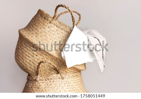 Straw wicker basket and white natural cotton fabric, towel on gray background. Fashionable bamboo basket stylish interior item eco design handmade. Decor of home. Natural eco materials, storage basket