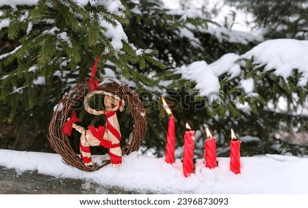 straw Yule Goat, burning candles in snow outdoor. Winter nature background. Traditional festive decor, Symbol of Scandinavian, Northern European Yule, Christmas holidays. Winter ritual for Yuletide