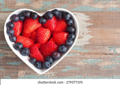 Strawberries and blueberries arranged in a heart shaped bowl on a rustic wooden table. These super-food berries are part of a healthy diet promoting a healthy heart and well being.