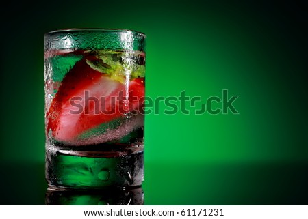 Strawberries in a glass. A slice of fresh red berry in a cold small glass on a green background. Freezing fruits to wash your face in the morning.